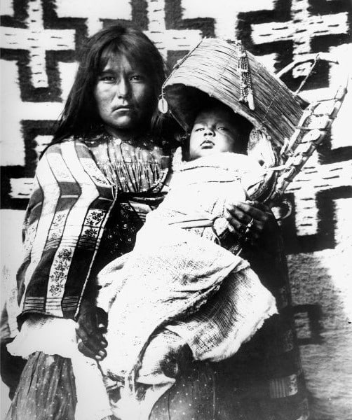 photo noir et blanc d'une mère indienne d'amérique du Nord avec son bébé en portage dans une sorte de nacelle en bois