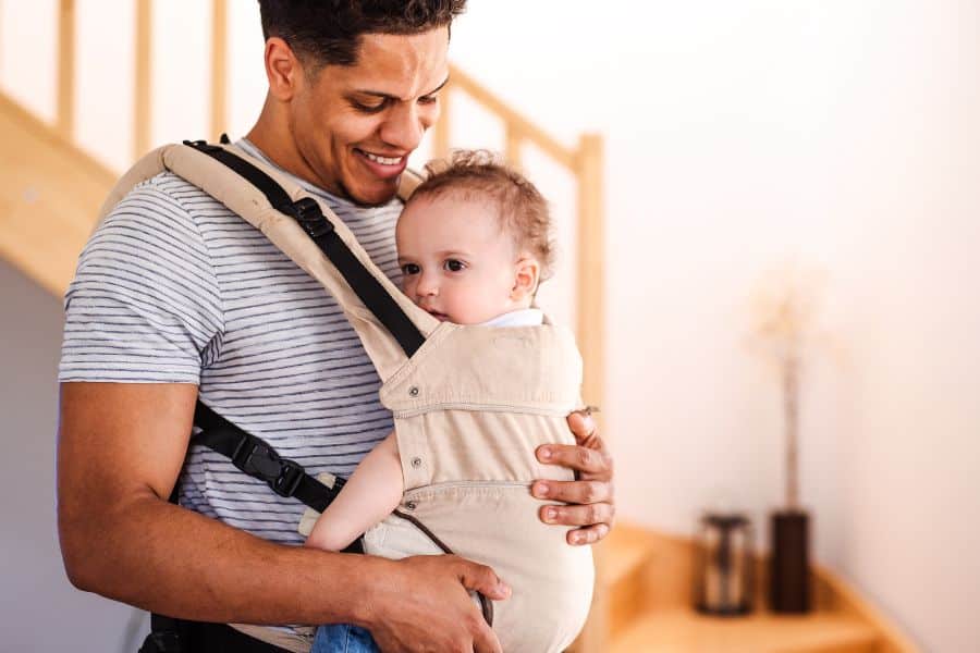 Père souriant portant bébé dans un porte-bébé préformé.